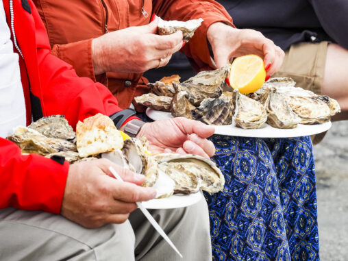 Elderly man and woman eating oysters from paper plates with lemon wedges on the side